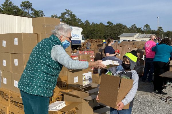 Volunteer helps young boy with preparing food box.
